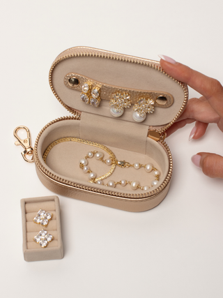 Small champagne jewellery case open with bracelet and pearl jewellery inside, removable ring insert placed beside the case.