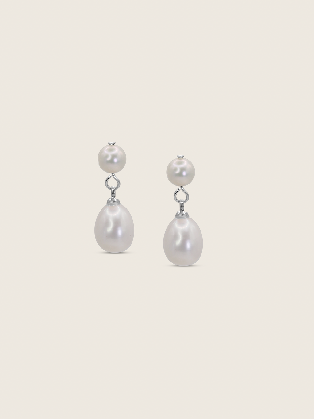 Flatlay of white gold drop earrings with round and teardrop freshwater pearls on a neutral background