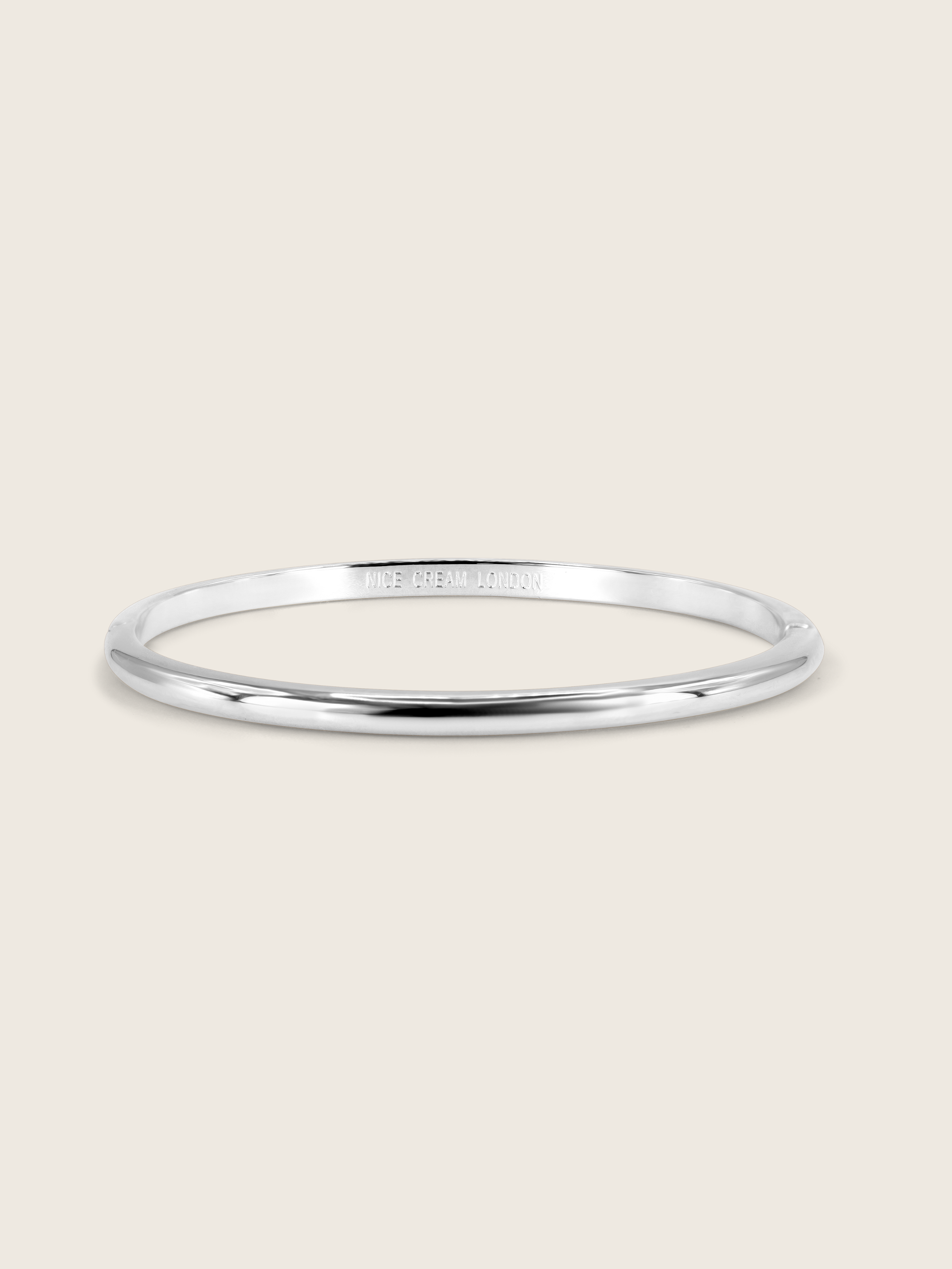 White gold plated slim Christy bangle on white background. Sleek and simple bangle with polished surface, perfect for minimalist jewellery styling.