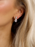 close-up of white gold plated Elodie earrings with an oval cut stone dangle design, worn in ear by a model