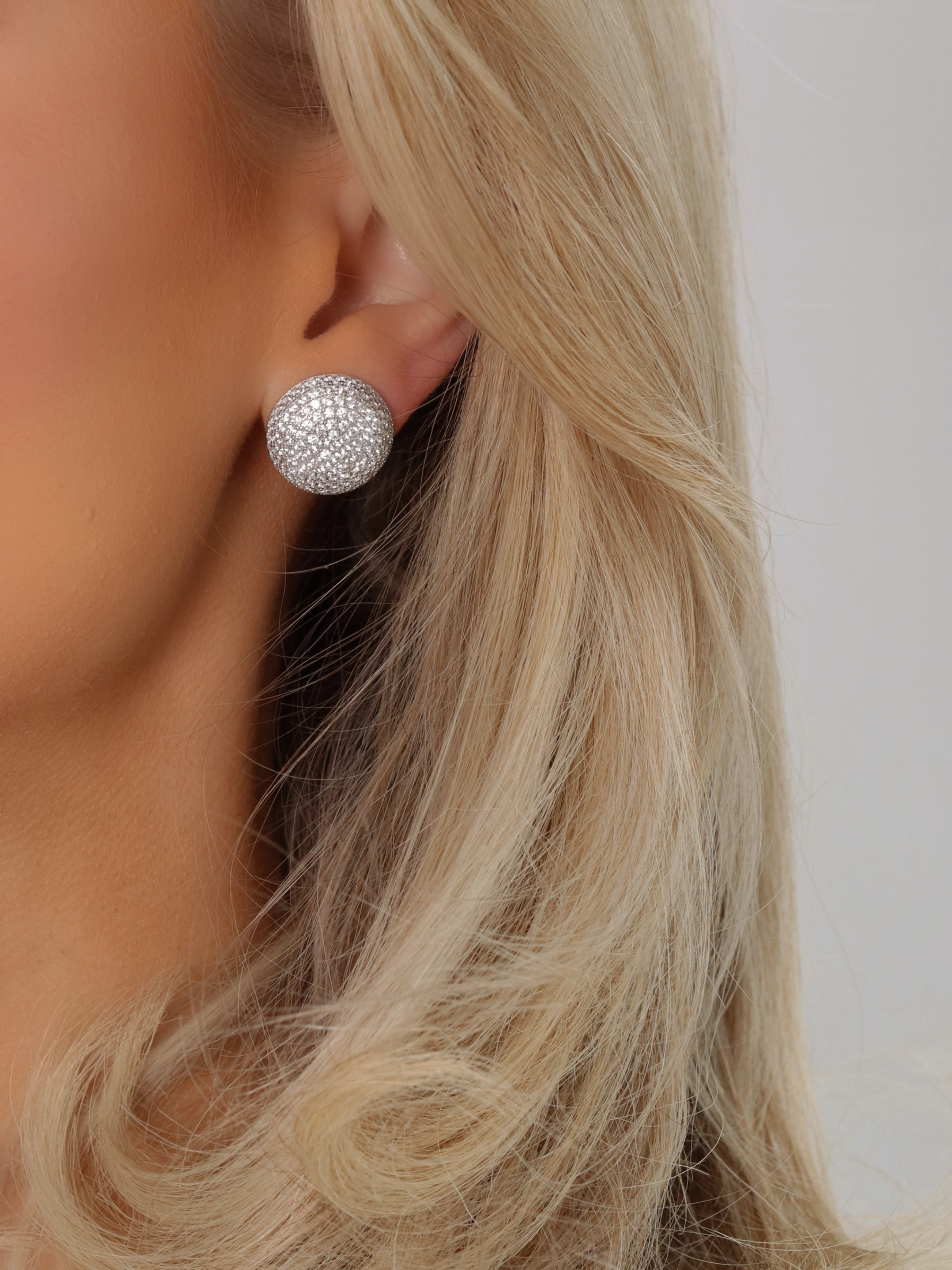 Close-up of model wearing round white gold plated stud earrings encrusted with pavé cubic zirconia stones
