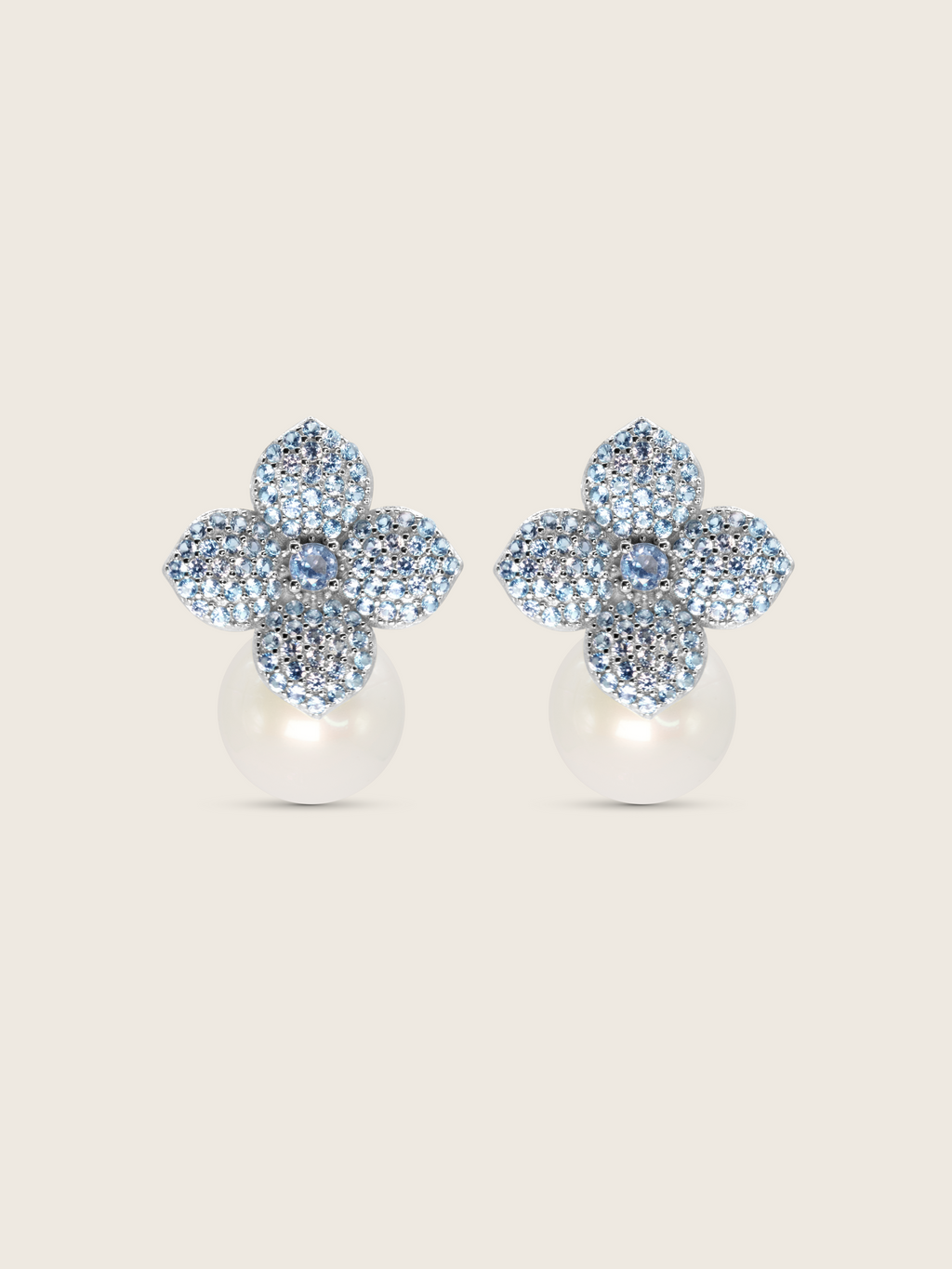 White gold plated hydrangea flower earrings with light blue cubic zirconia and shell pearl drop on white background. Sparkly floral stud earrings