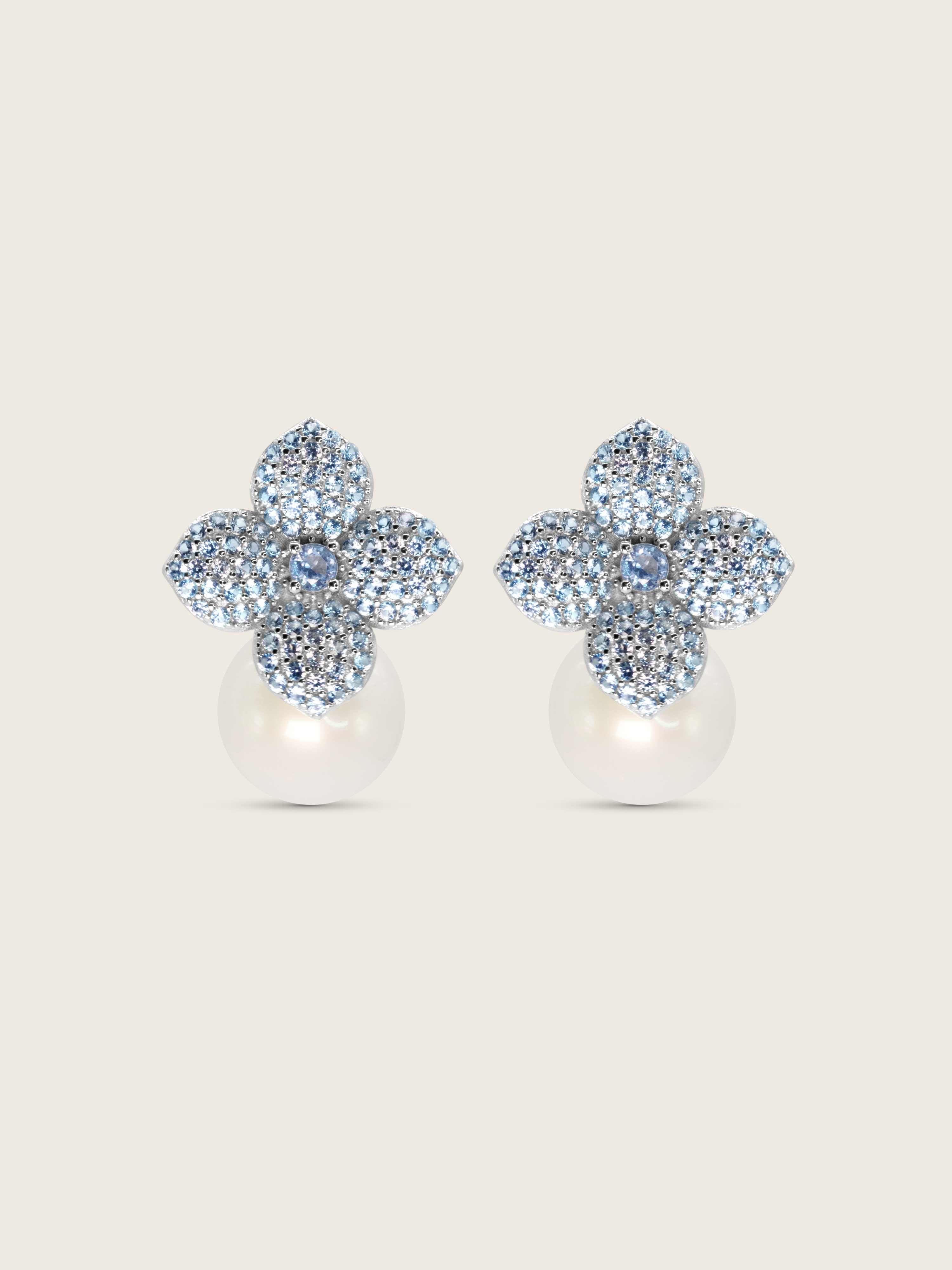 White gold plated hydrangea flower earrings with light blue cubic zirconia and shell pearl drop on white background. Sparkly floral stud earrings