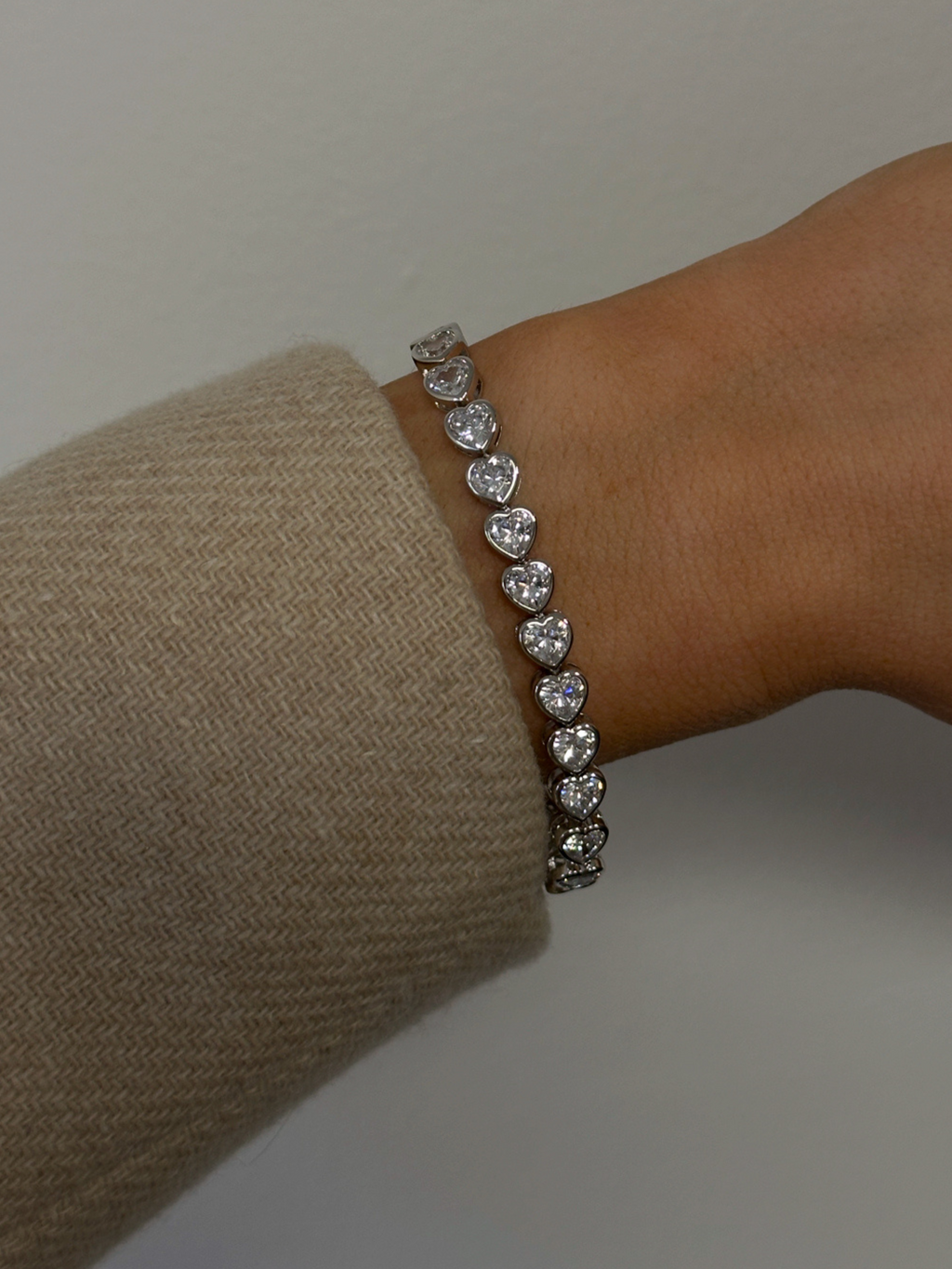 Juliette heart tennis bracelet in white gold with sparkling CZ stones, worn on wrist with a soft neutral knit for a chic everyday-luxe look
