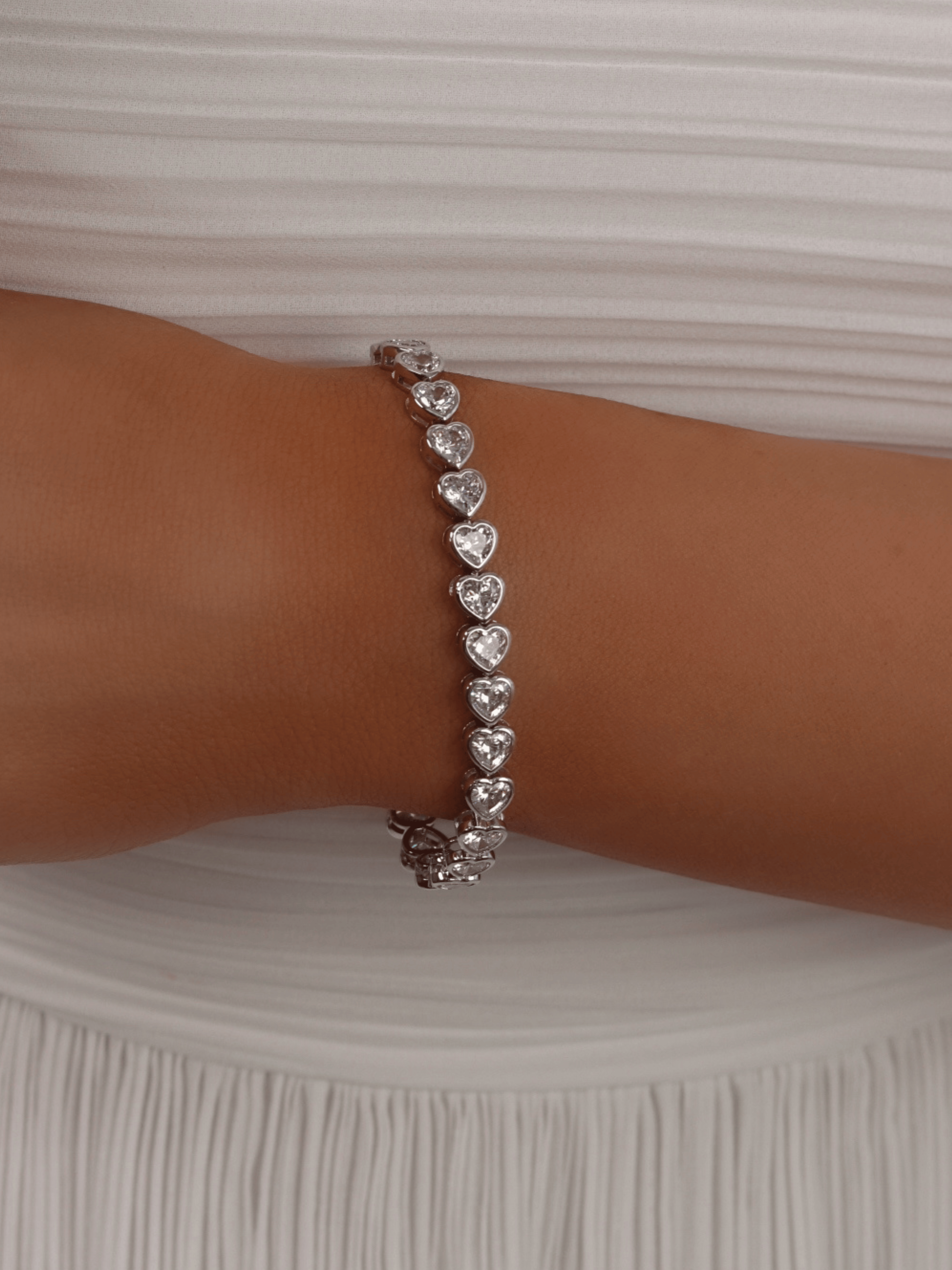 White gold plated bracelet with heart-shaped CZ stones, styled on model with pleated white dress - perfect for formal occasions or bridal elegance